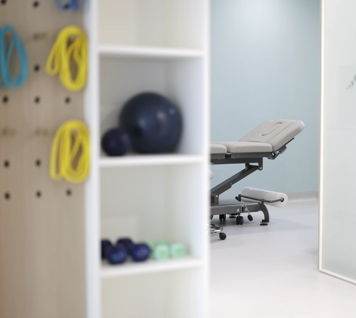 Physiotherapy room with treatment table, exercise balls and resistance bands for rehabilitation.