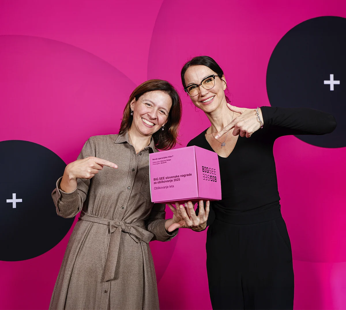 two ladies point at big see award on the stage